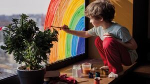Niño trabajando su desarrollo psicosocial de su hijo con pintura de un arcoíris en la ventana
