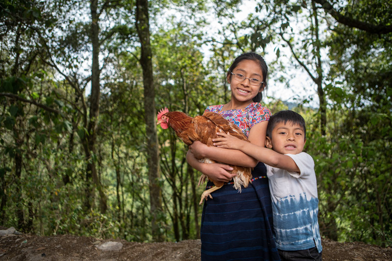 Hermanos posan cargando una gallina.