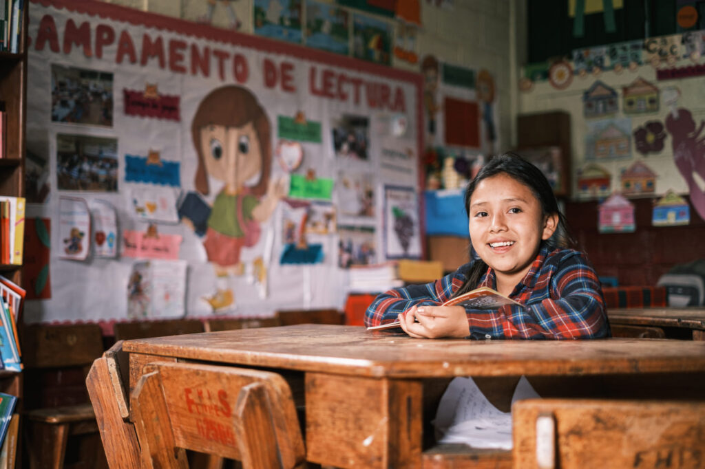 niña sentada en una mesa en un salón de clases