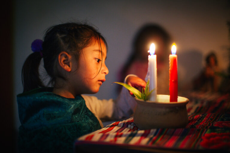 Niña encendiendo una vela durante el Adviento, simbolizando esperanza y protección para los niños.